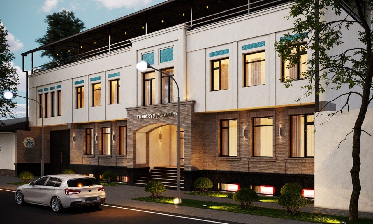 The Academy on Segoh street at dusk: two floors of pale plaster and brick, turquoise tile set above the windows, and warm light in every room.