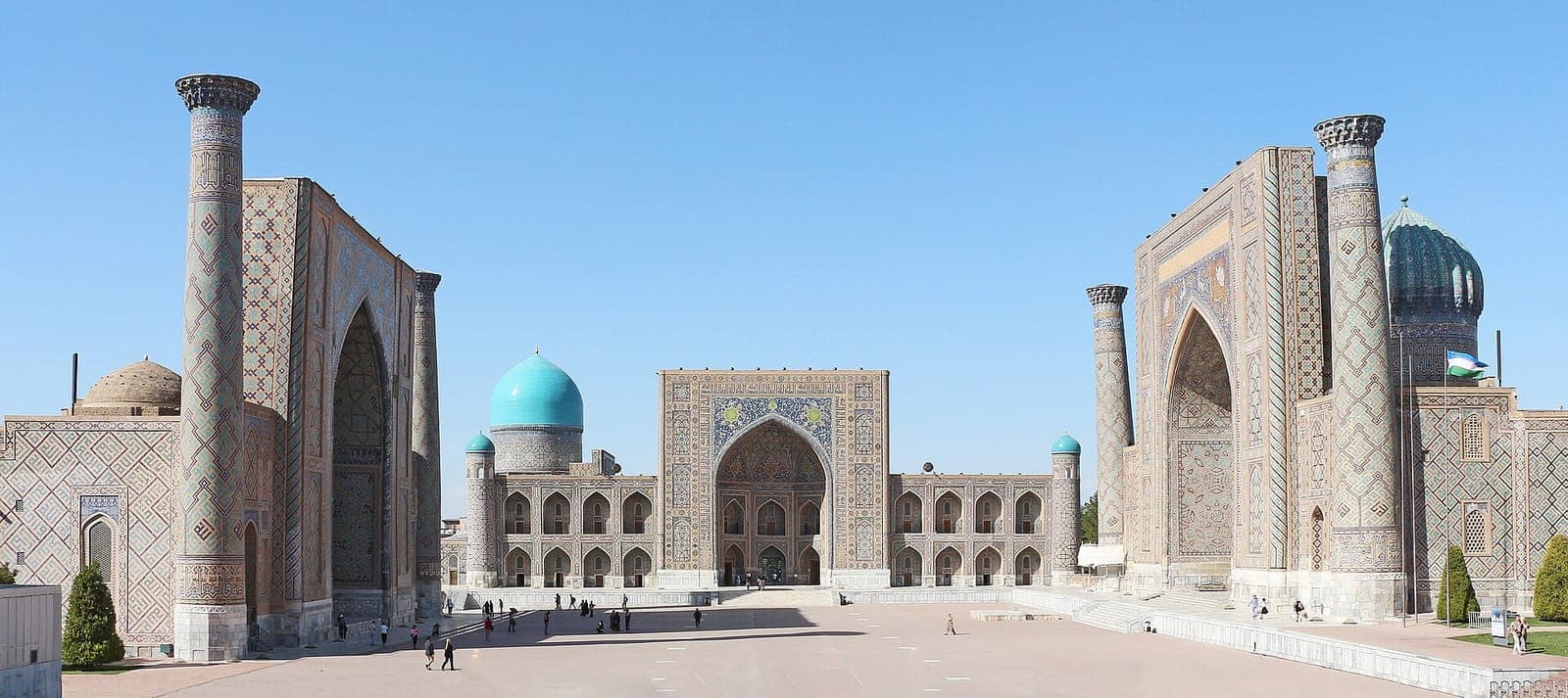 The Registan in Samarkand: three tiled madrasas facing a wide square, their portals and turquoise domes rising against a clear sky.